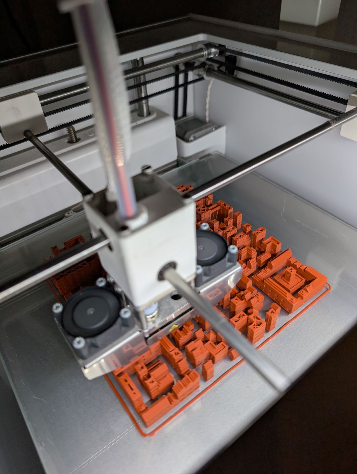 A city being printed: the print head above rows of small orange buildings